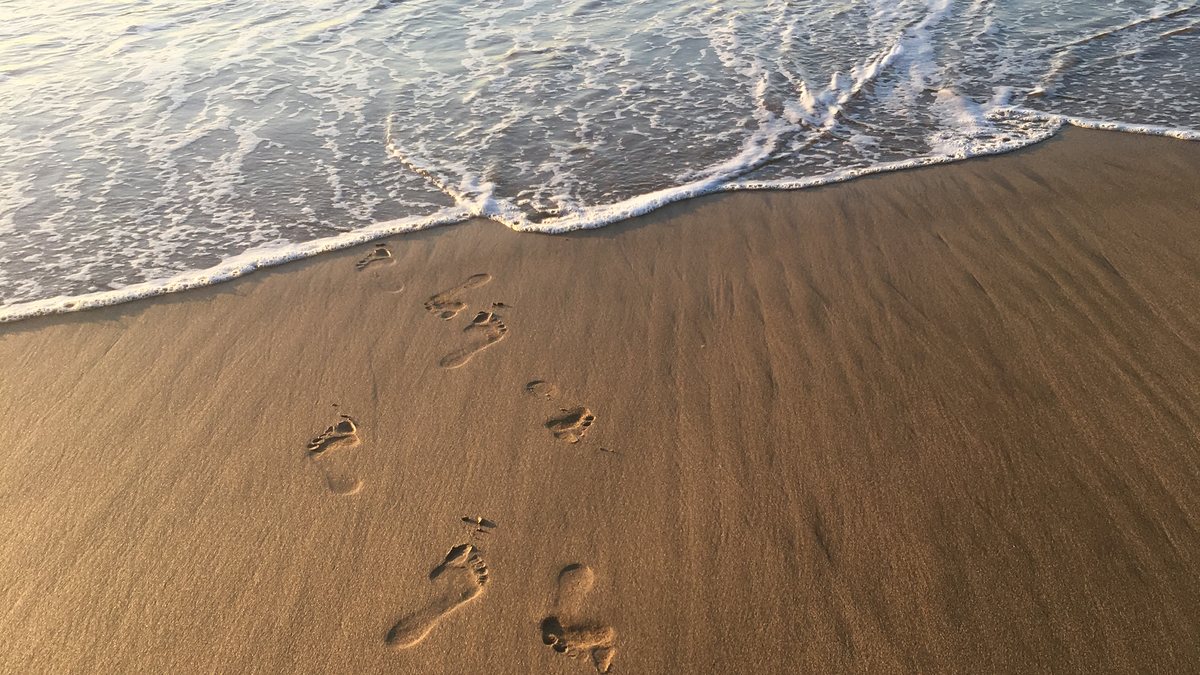 A trail of footprints in wet sand beside the incoming tide