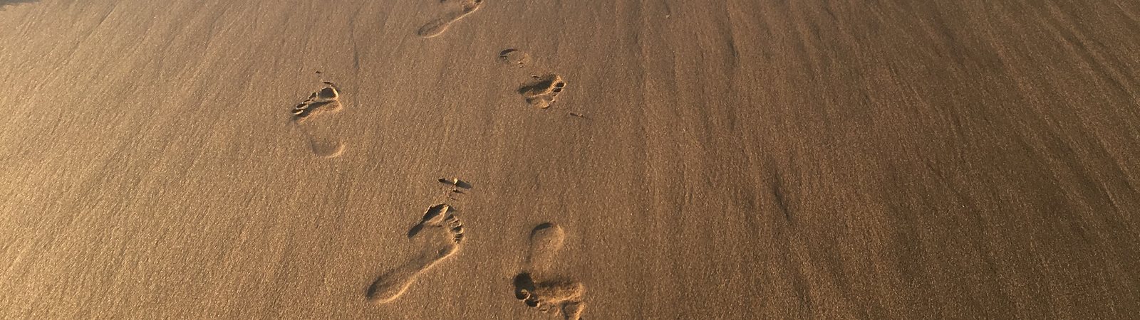 A trail of footprints in wet sand beside the incoming tide